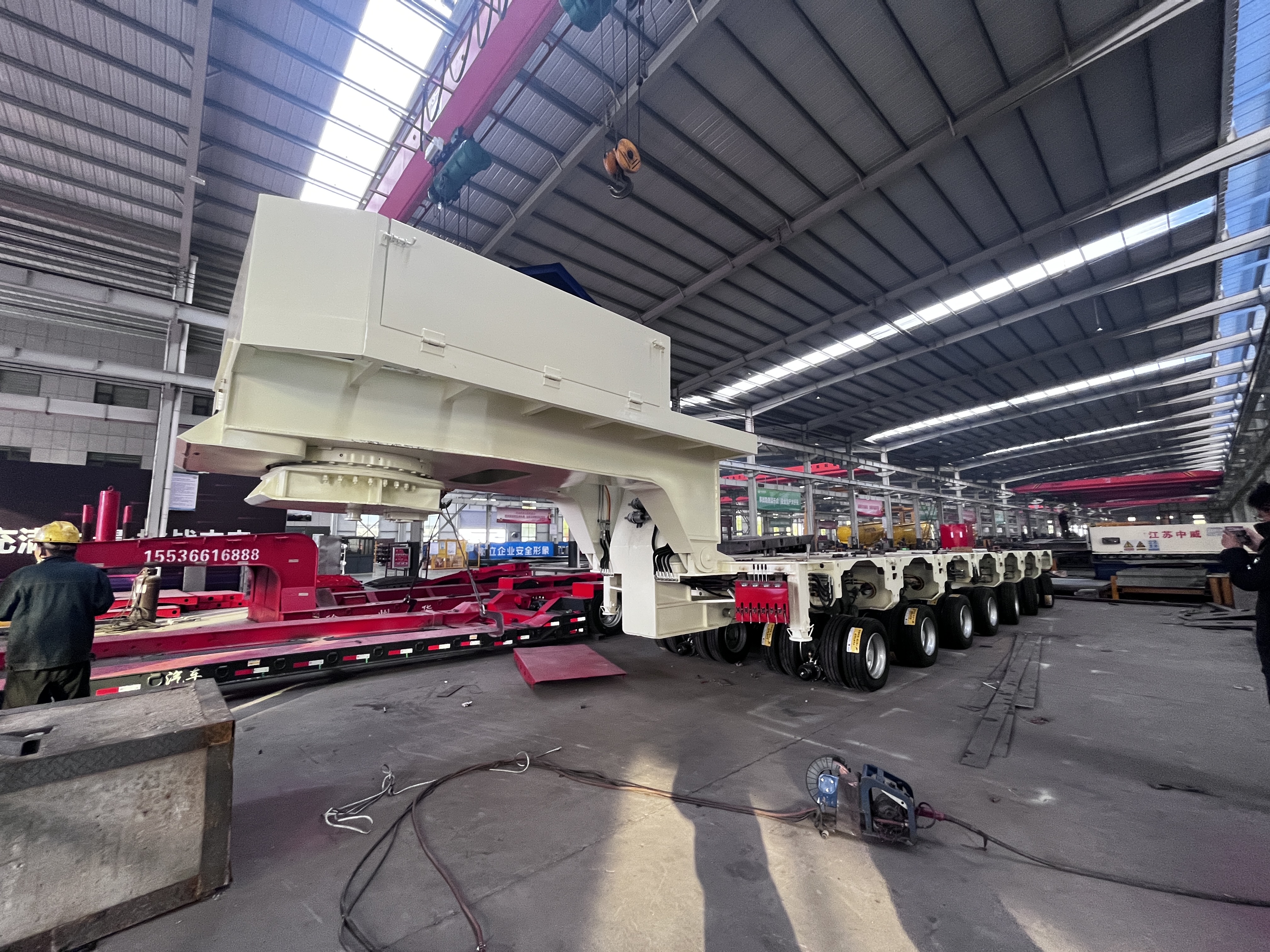 Overhead crane assembling the heavy-duty gooseneck unit onto a multi-axle modular hydraulic trailer in the HUAYUE manufacturing facility