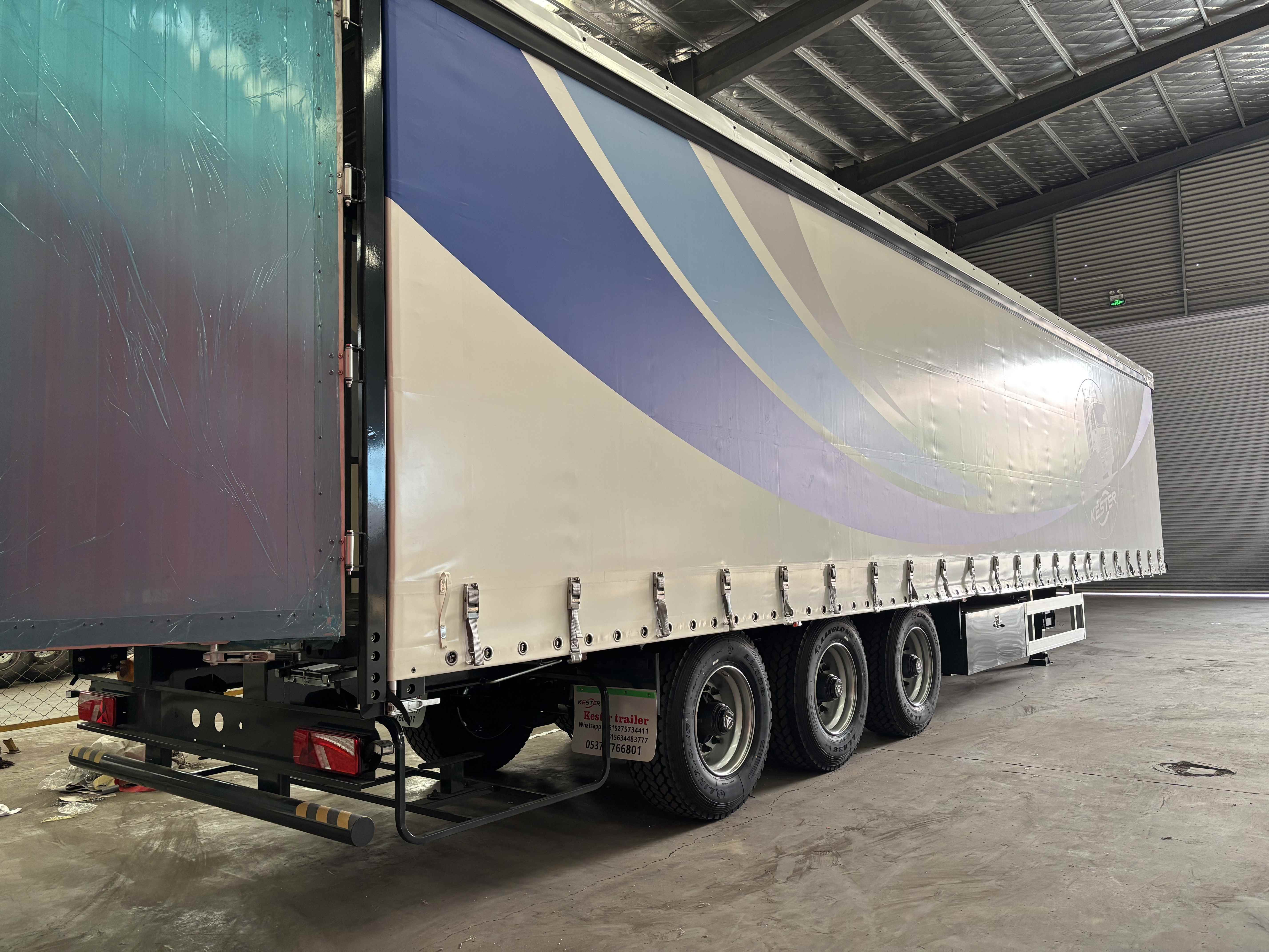 Rear-side view of a 3-axle curtain slider trailer showing the robust rear door and the heavy-duty triple axle suspension system