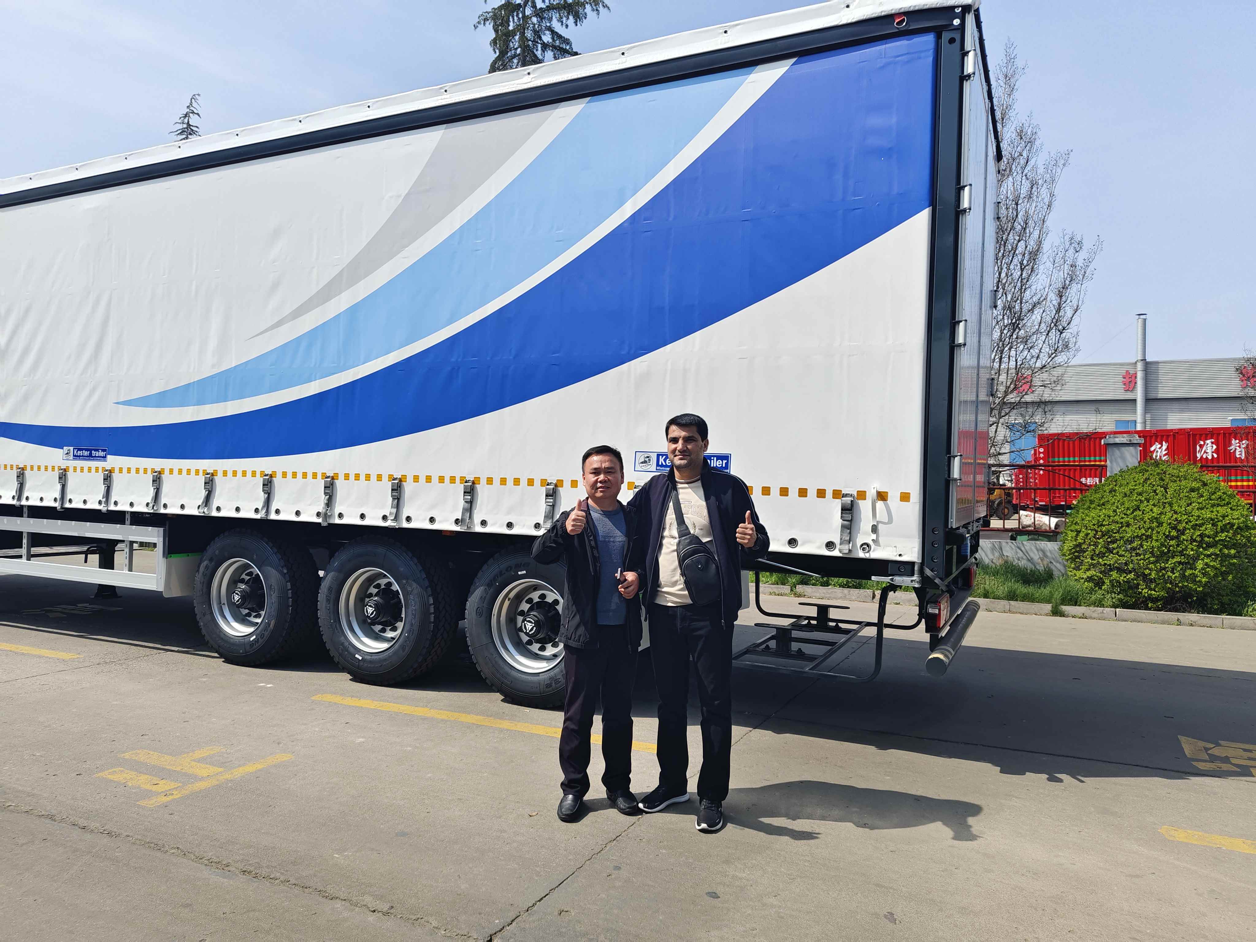 A Philippines client giving a thumbs up with a HUAYUE representative in front of a brand new 3-axle curtain side trailer during a factory inspection