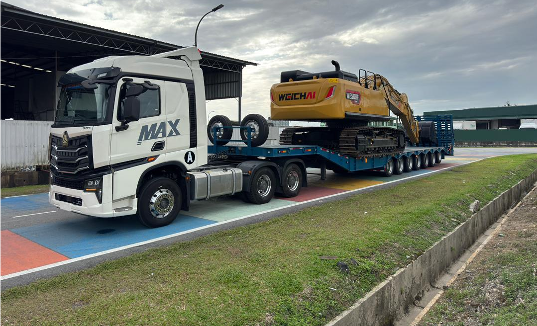 Client feedback photo showing a white truck towing a blue HUAYUE 7-axle heavy-duty trailer loaded with a large excavator on the road