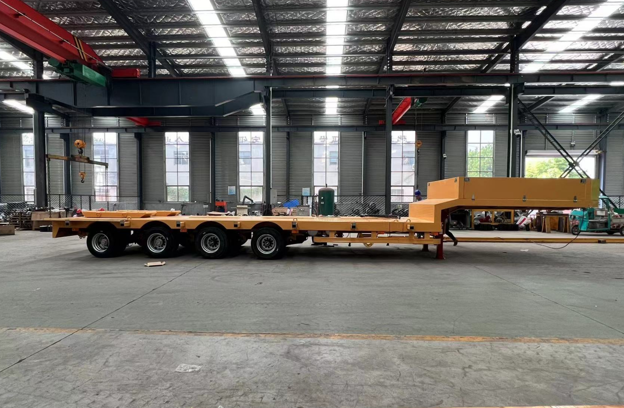 Side profile of HUAYUE 4-axle European standard lowbed trailer in the factory, featuring a long working deck and multi-axle configuration for heavy transport.