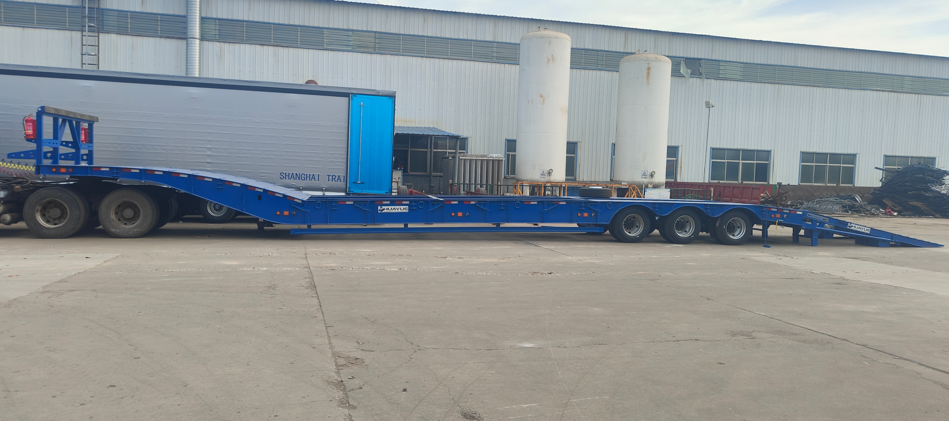 Full side profile of the HUAYUE 3-axle heavy-duty standard lowbed trailer, featuring a high-strength fixed gooseneck, an ultra-long working deck, and fully lowered double-folding hydraulic ramps for an extremely low-angle loading corridor.