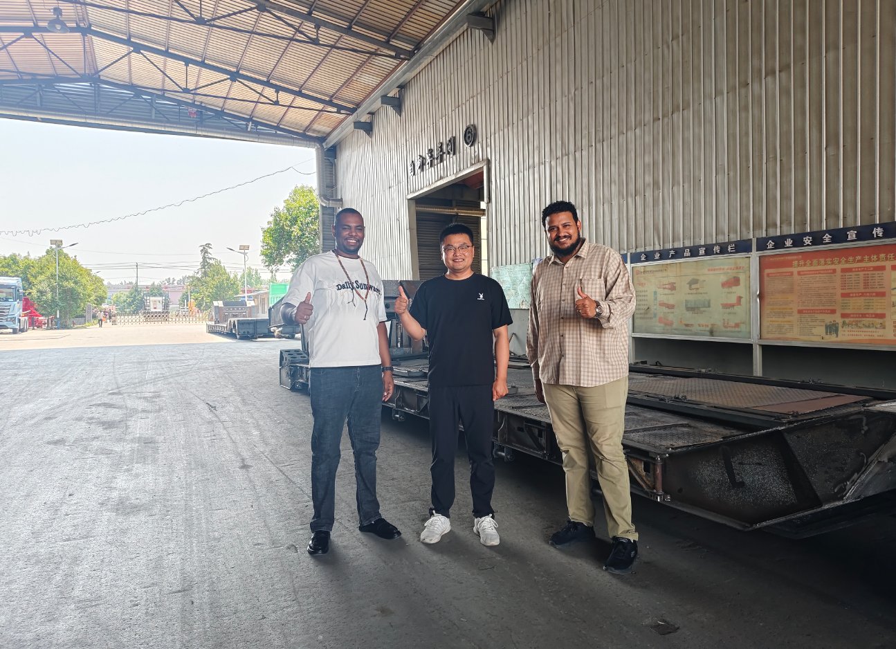 Representatives from a Vietnamese heavy transport fleet conducting a live factory inspection at HUAYUE, posing with our engineers in front of a heavy-duty lowbed chassis to witness true manufacturing strength.