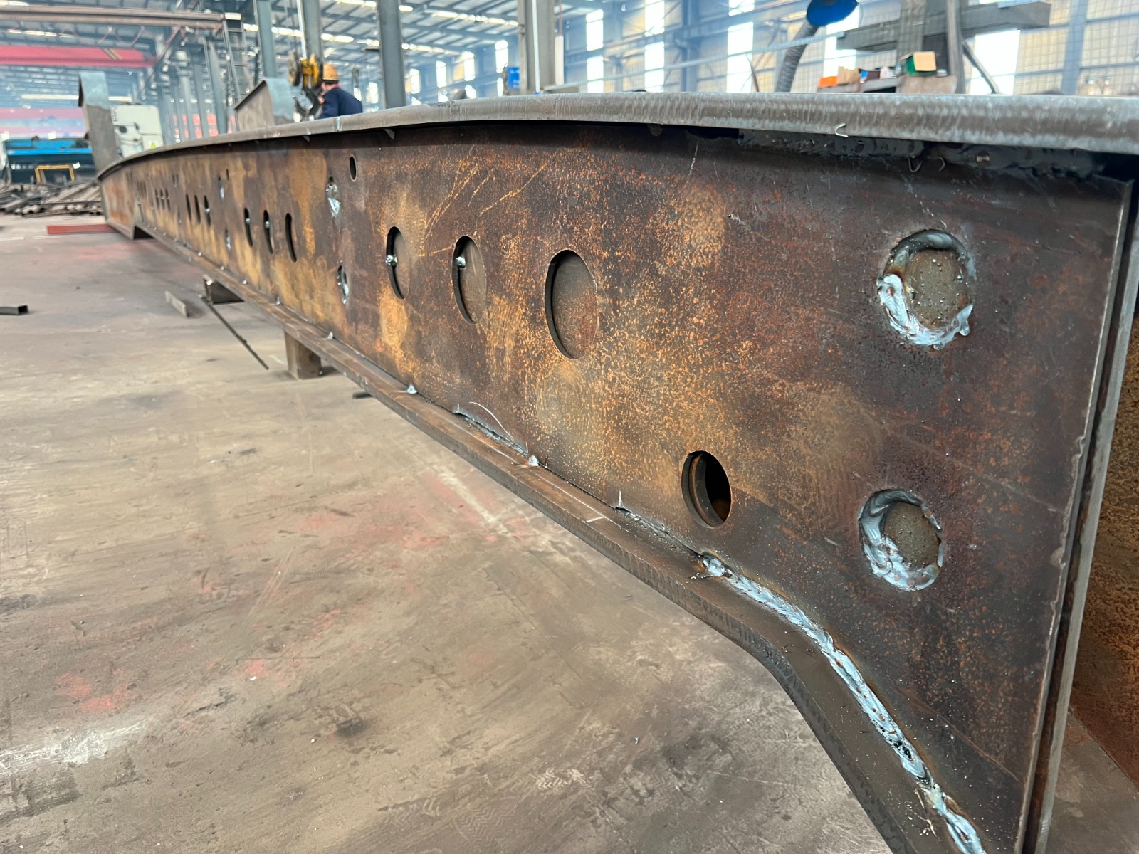 Real shot of HUAYUE heavy-duty trailer main beam web cut-outs, featuring precision welded reinforcement rings on the edges, scientifically located on the neutral axis to reduce tare weight while maintaining extreme tensile and torsional rigidity.