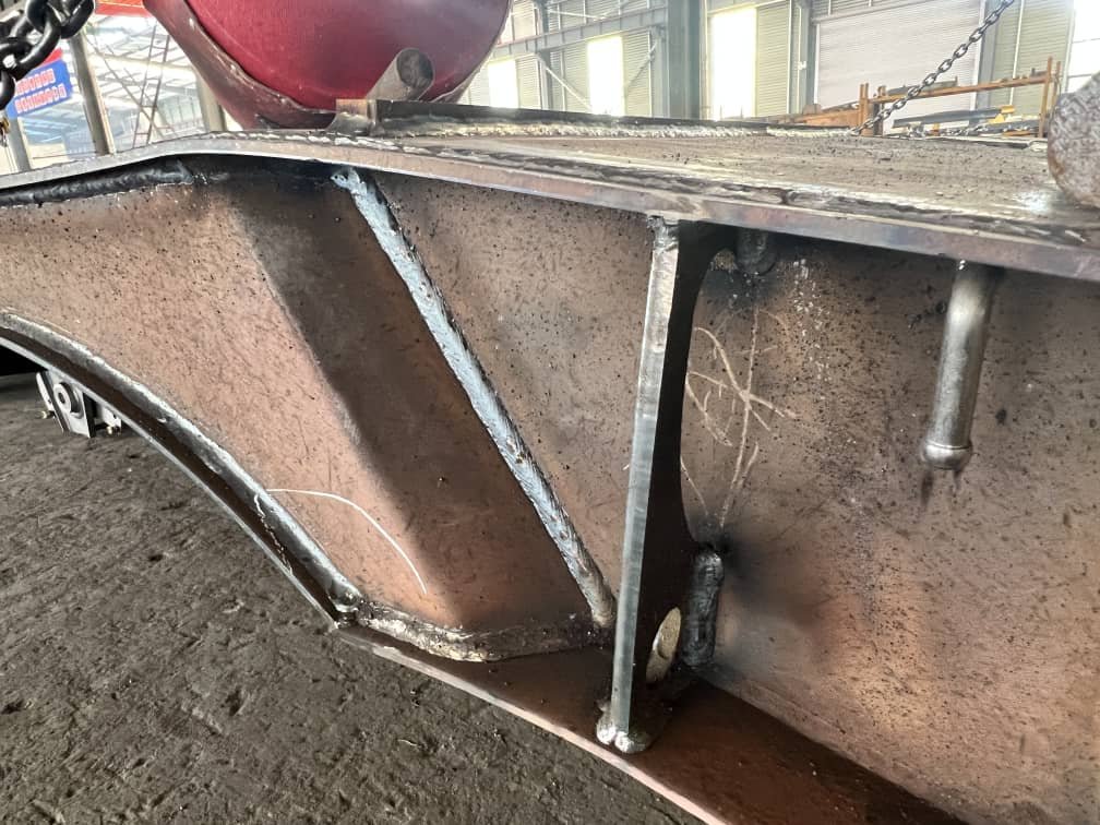Precision welding details of the main beam web and vertical stiffeners on a heavy-duty trailer, complementing the automated double-sided submerged arc welded main beam to form a torsion-resistant chassis structure meeting X-ray flaw detection standards.