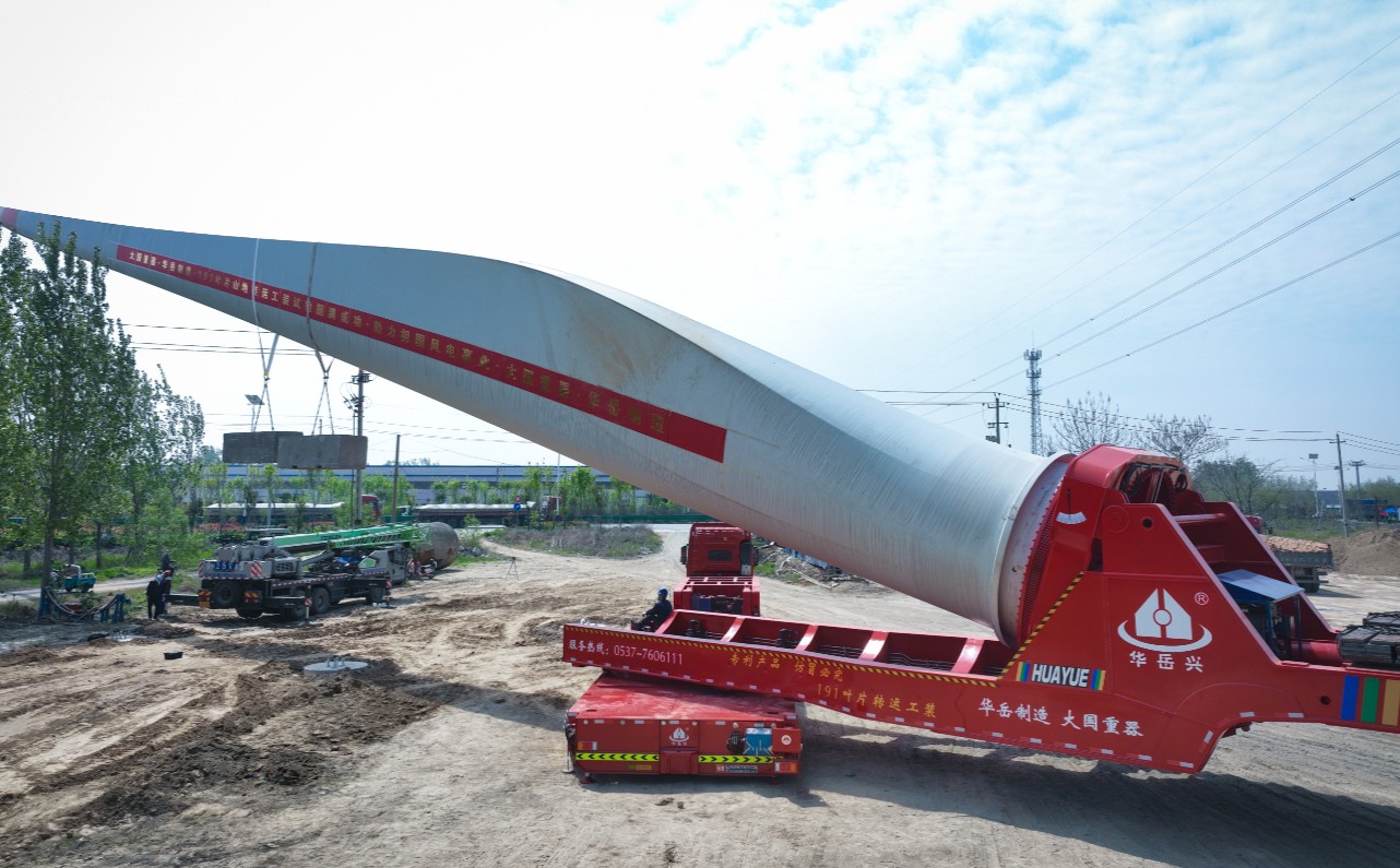 HUAYUE Wind Turbine Blade Lifter Adapter Trailer operating at a mountain wind farm, raising a massive rotor blade to bypass terrain obstacles.