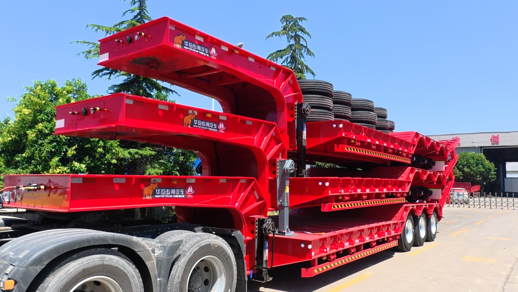 Stacked red HUAYUE 3-axle lowbed special trailers, equipped with heavy-duty mechanical leaf spring suspensions built for harsh conditions, ready for overseas export.