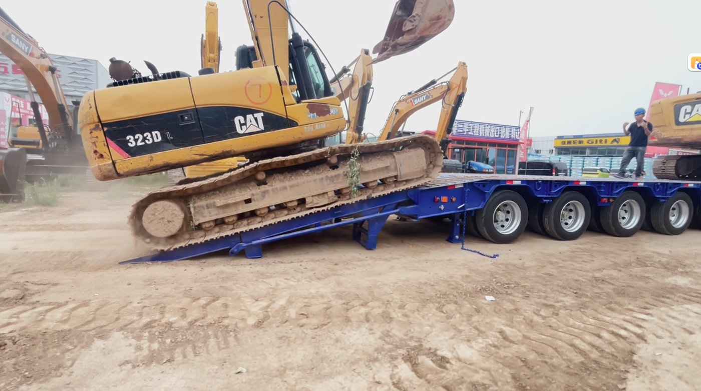 A photo showing a massive excavator loaded on a standard high-deck trailer, looking unstable or barely squeezing under a bridge. This instantly highlights the customer's pain point.