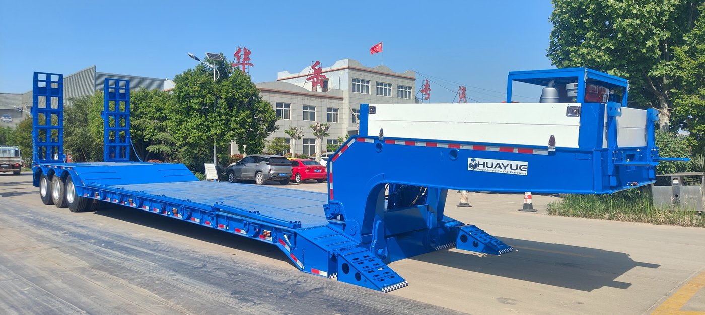 A photo showing the rear dual-folding hydraulic ramps fully extended to the ground, preferably with a wheel loader or excavator just starting to drive up the gentle slope.