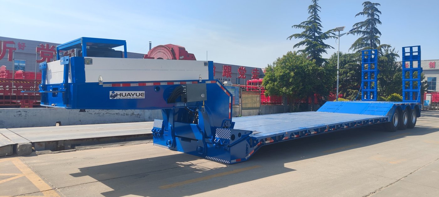 Heavy machinery safely and smoothly driving onto the deck via the front ground-level ramp of a HUAYUE RGN semi-trailer, perfectly showcasing the technical advantages of front loading in preventing bottoming out and track slipping.