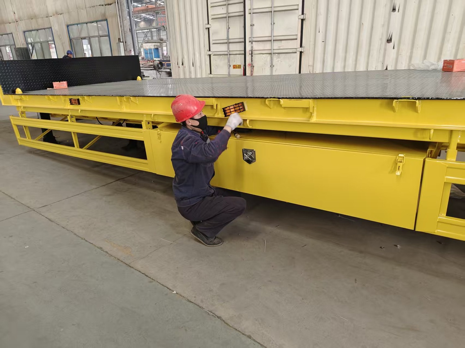 Yellow lowbed trailer in a factory with a worker attending to the side structure