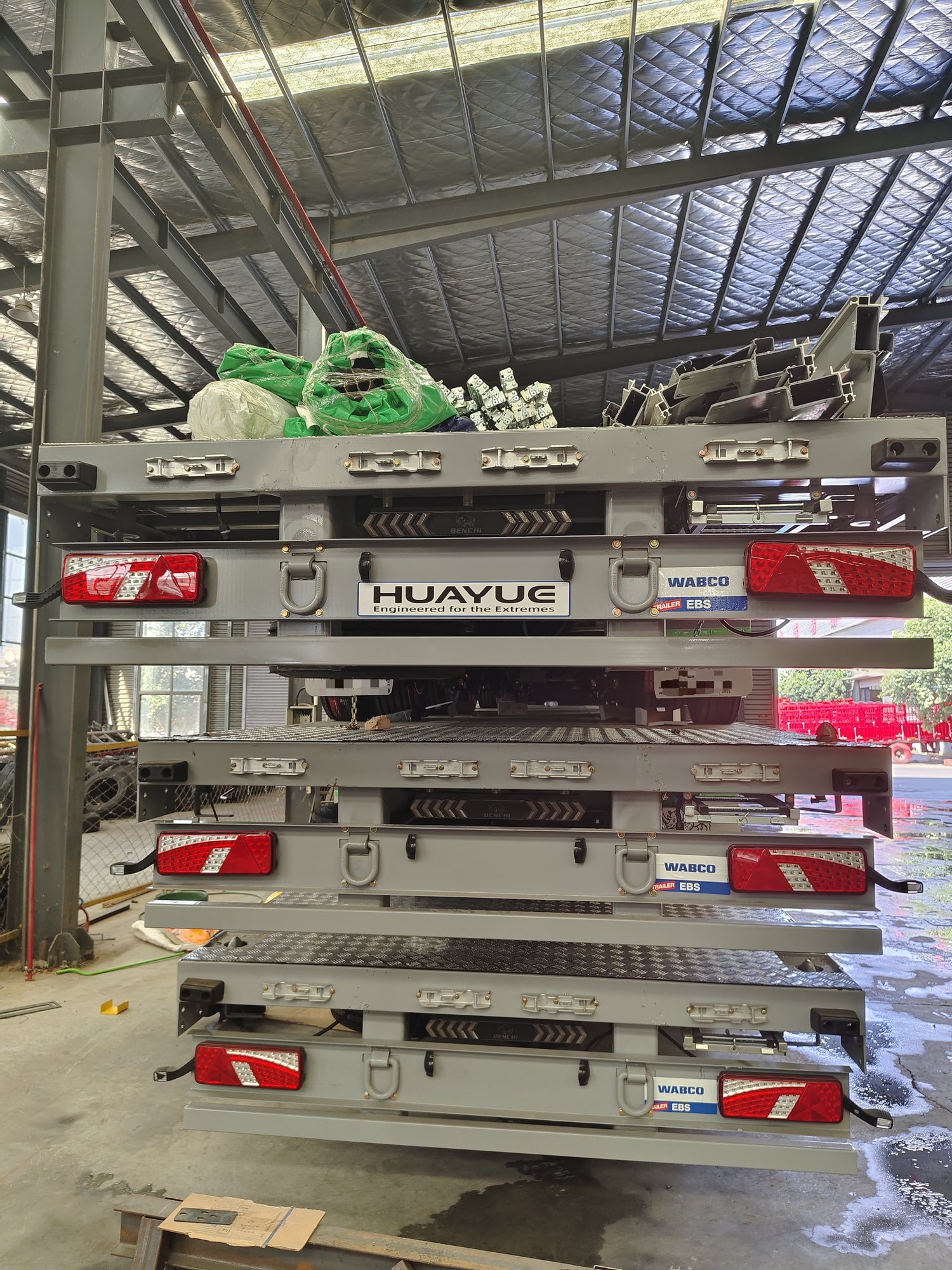 Rear view of stacked Huayue curtainsider trailer sections with visible lights and component labels during shipping preparation