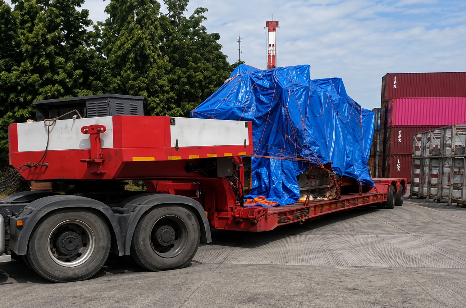 Covered load on a red removable-gooseneck trailer in a container yard