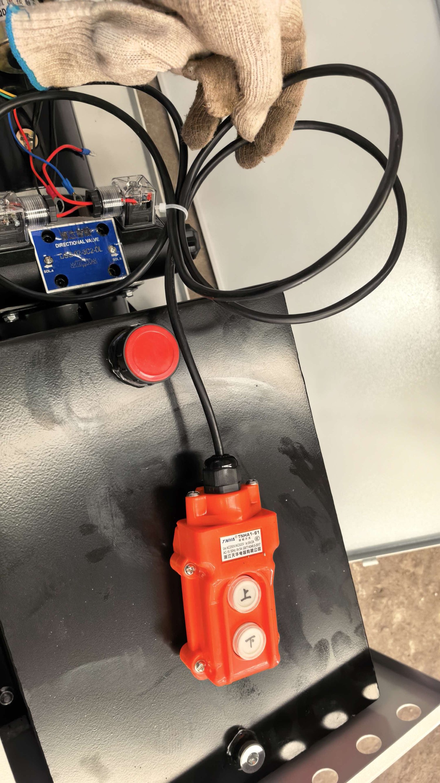 Red wired pendant control beside a directional valve in a hydraulic system enclosure