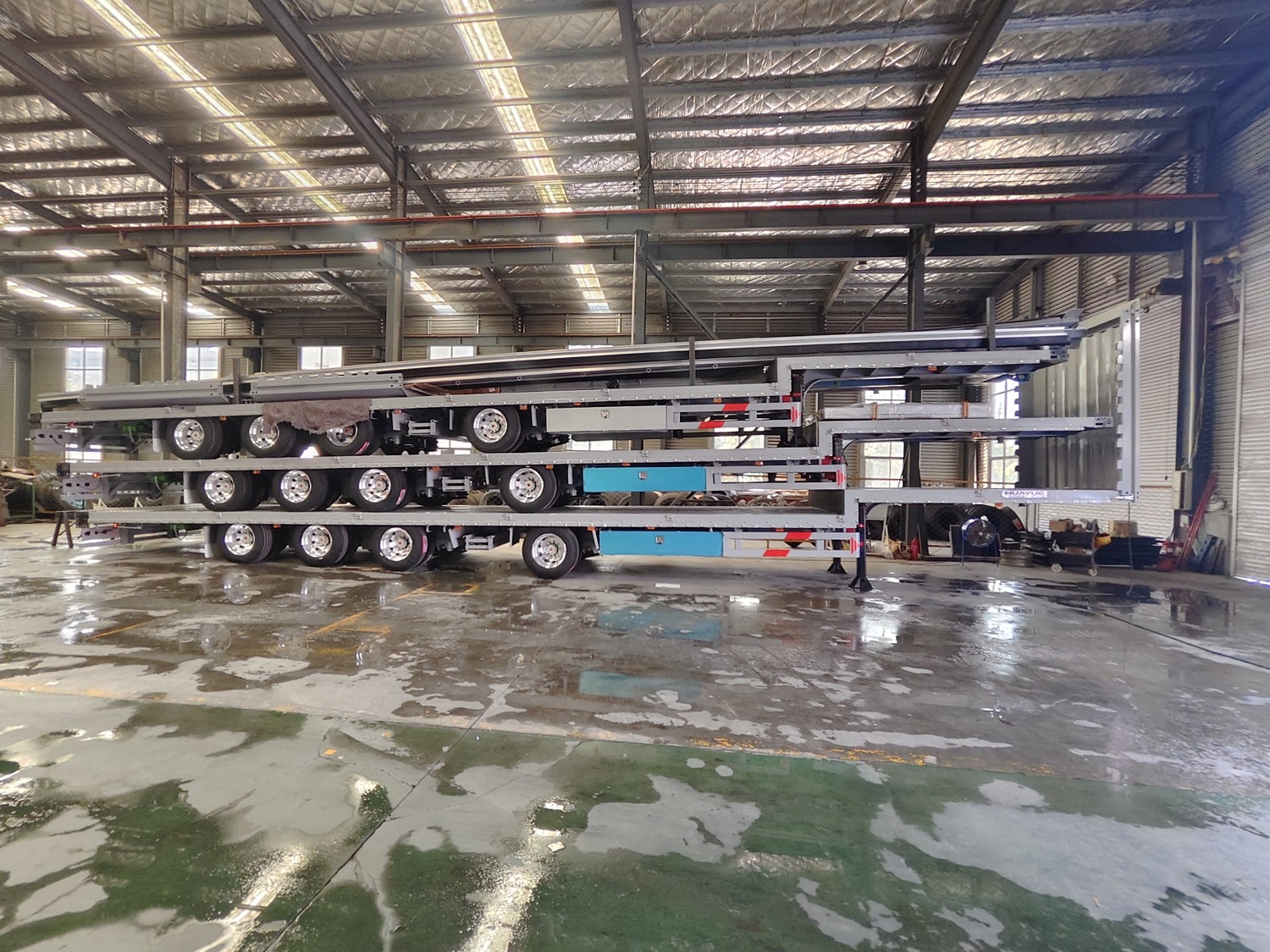 Side view of three disassembled Huayue 4-axle curtainsider semi-trailer units stacked in the factory