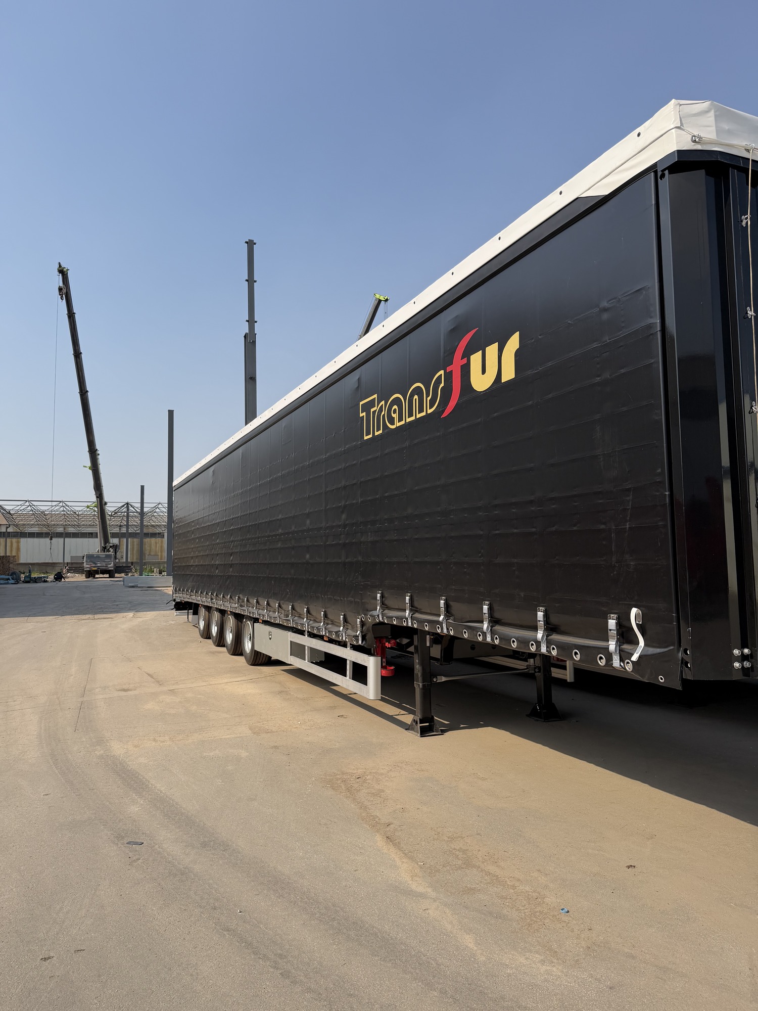 Side view of a black curtain side semi-trailer in a factory yard